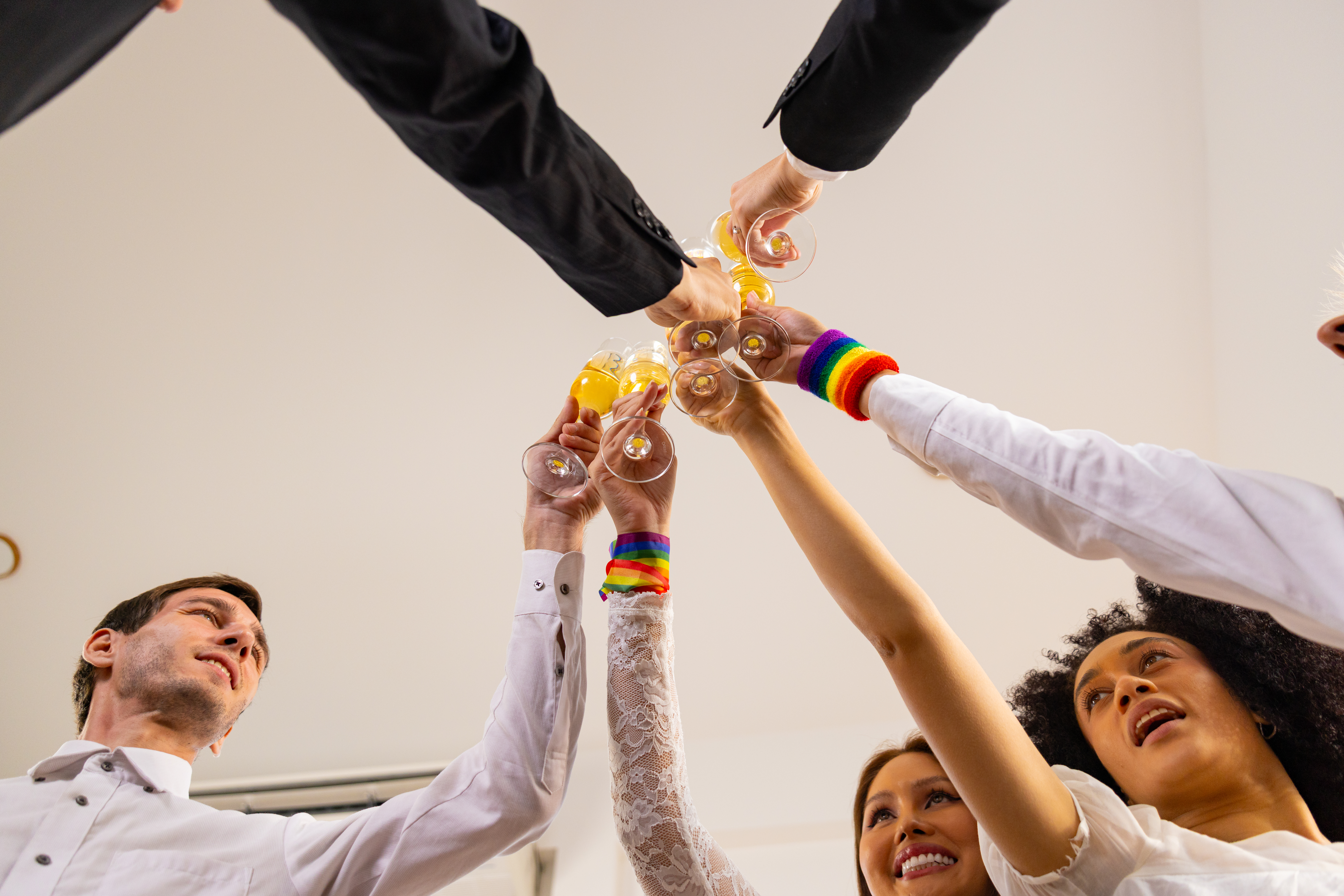 Friends raising glasses together, including people wearing rainbow Pride wristbands